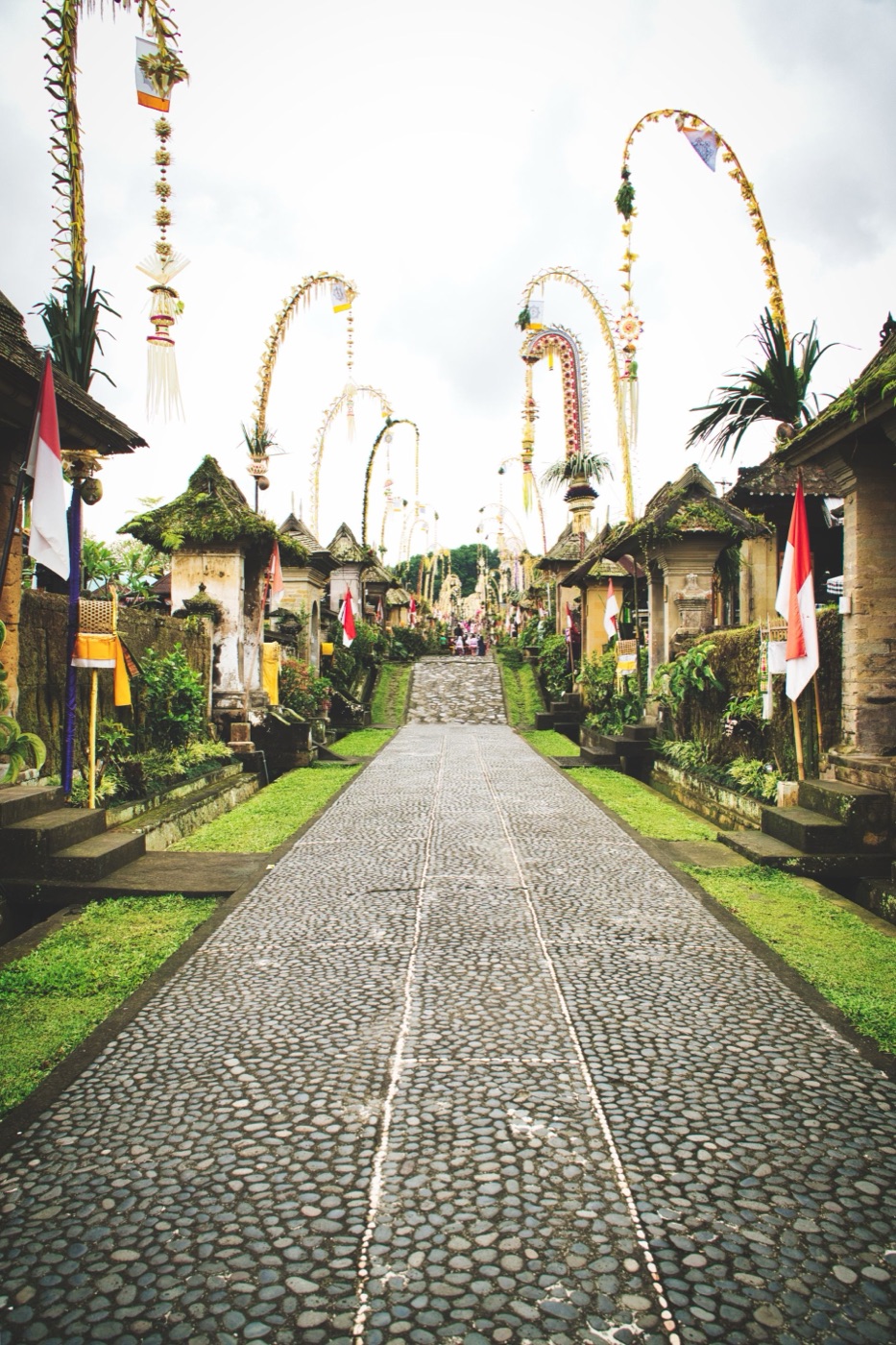Traditional Balinese penjor poles arching over a village street during a cultural ceremony.